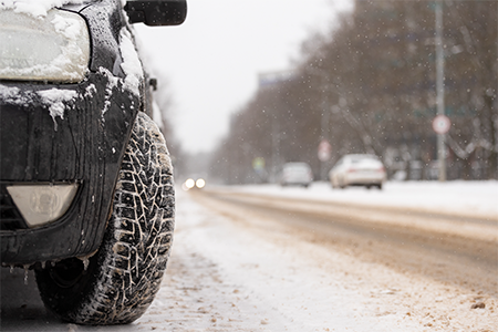 black car parked on a slushy road in the winter with snow falling