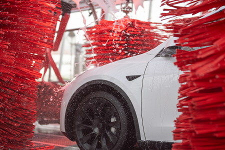 White Tesla sedan between red car wash brushes in Tommy's Express Car Wash